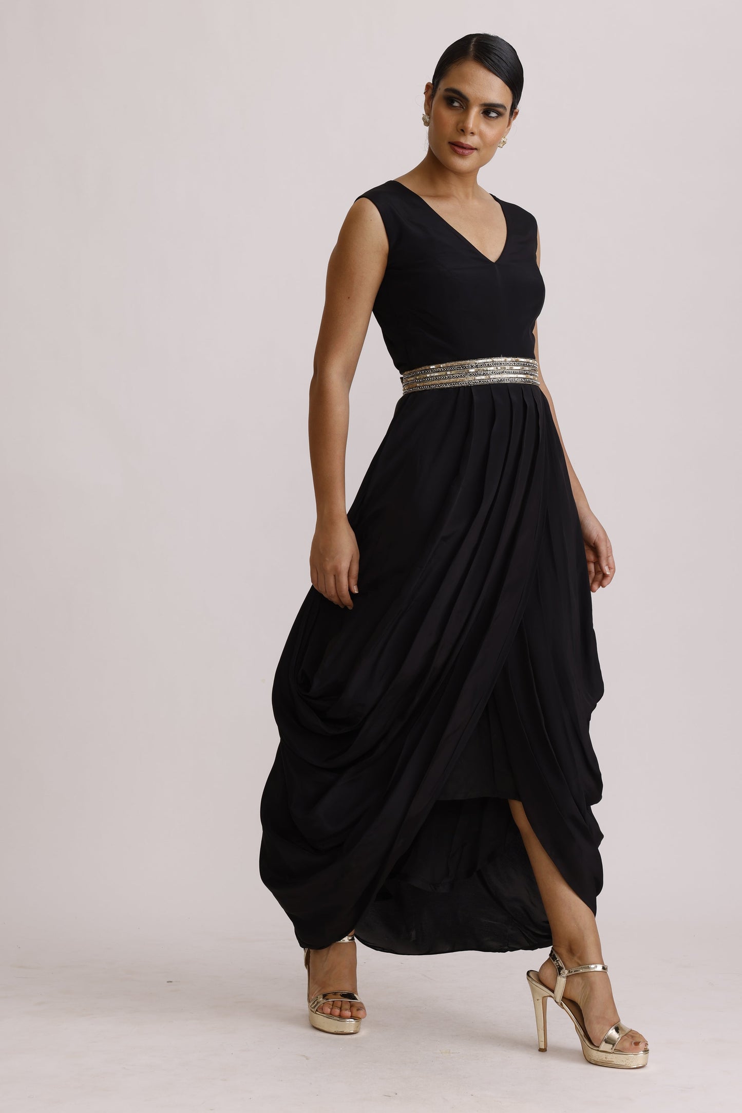A woman modeling a floor-length black gown with a silver beaded waistband, paired with beige high-heeled sandals, photographed against a plain light background.