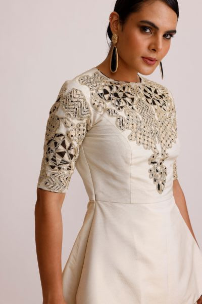 Woman wearing a cream-colored outfit with intricate lace detailing on a light background