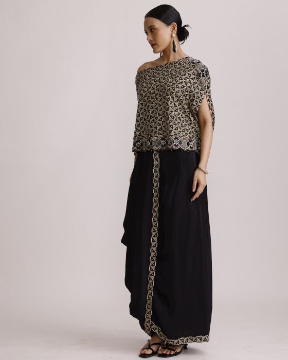 Woman wearing a patterned top and black pants with a decorative trim on a plain background