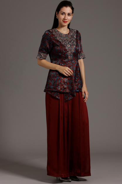 "Stunning Maroon Peplum Top in Pure Ajrakh Modal Silk with Intricate Embroidery on Yoke and Sleeves, Paired up with Maroon Pleated Pants in Crepe."