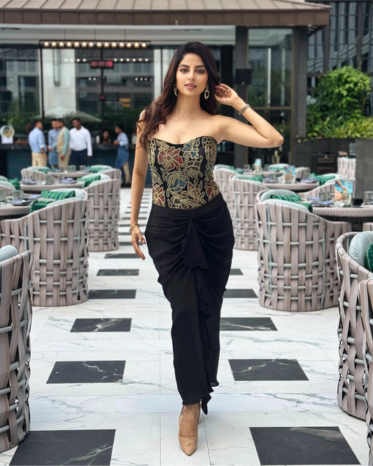 A Ekta Maru posing on an outdoor patio walkway, wearing a strapless corset-style top with a multicolor paisley pattern and black draped trousers.