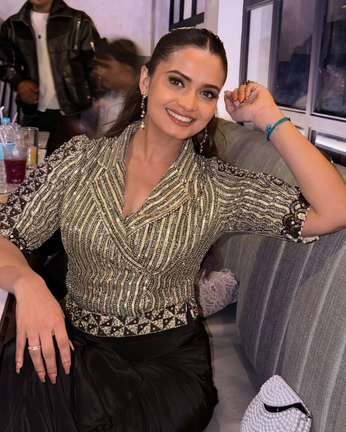 A Neelam Giri posing in a black and gold patterned wrap-style blouse with black skirt in a social setting.