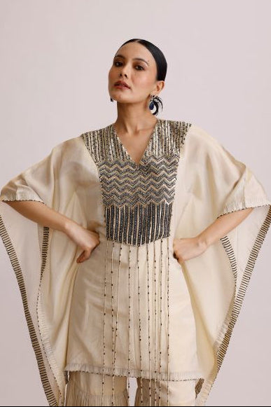 Woman wearing a traditional outfit with a patterned top and beige skirt on a plain background