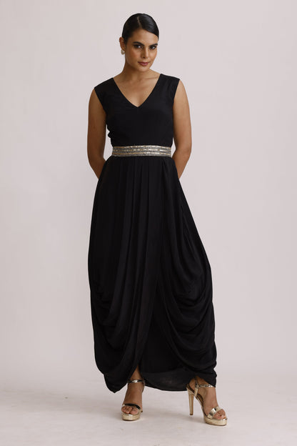 A woman modeling a sleeveless black floor-length gown with a silver beaded waistband, photographed against a plain light background.