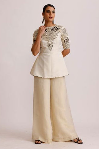 Woman wearing a cream-colored dress with intricate detailing on a plain background