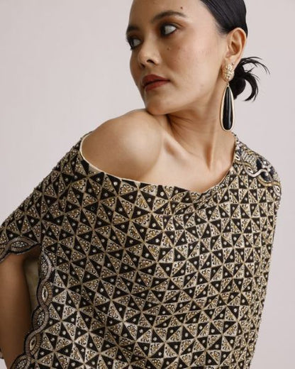 Woman wearing a black and gold patterned top with a plain background