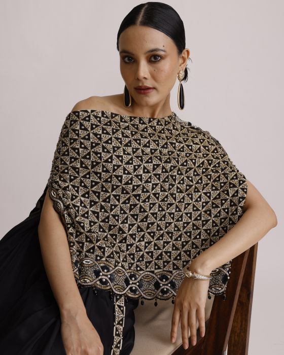Woman wearing a black and gold patterned top with a plain background