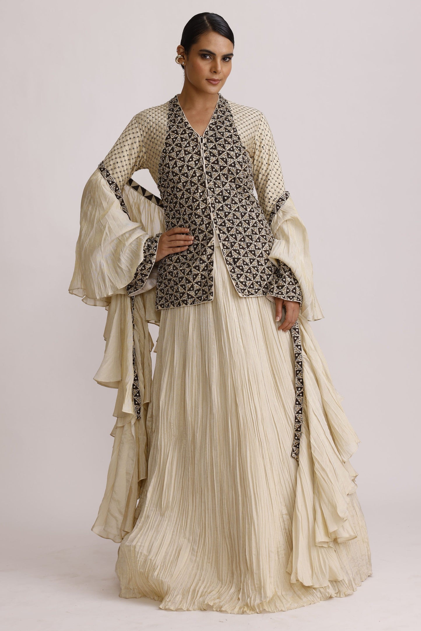 A model wearing a traditional South Asian outfit featuring a pleated cream-colored skirt and a patterned cream and black kurta, photographed against a plain light background.