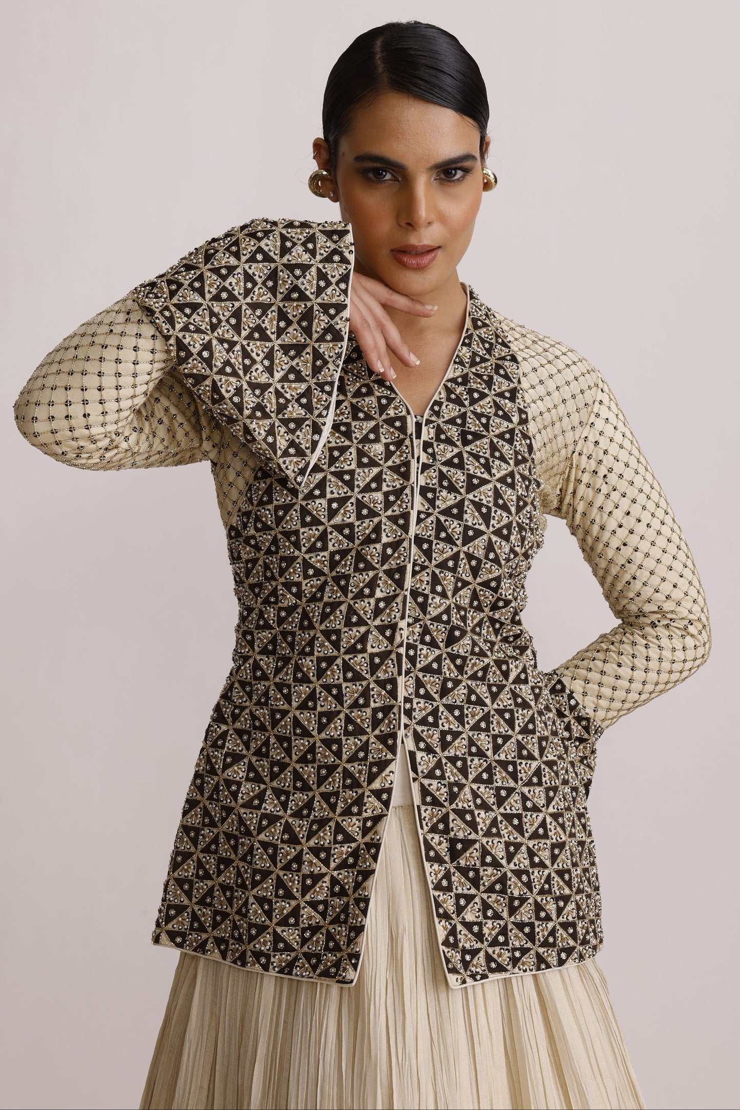 A model wearing a sleeveless geometric print vest over a cream-colored long-sleeve top, photographed against a solid light beige background.