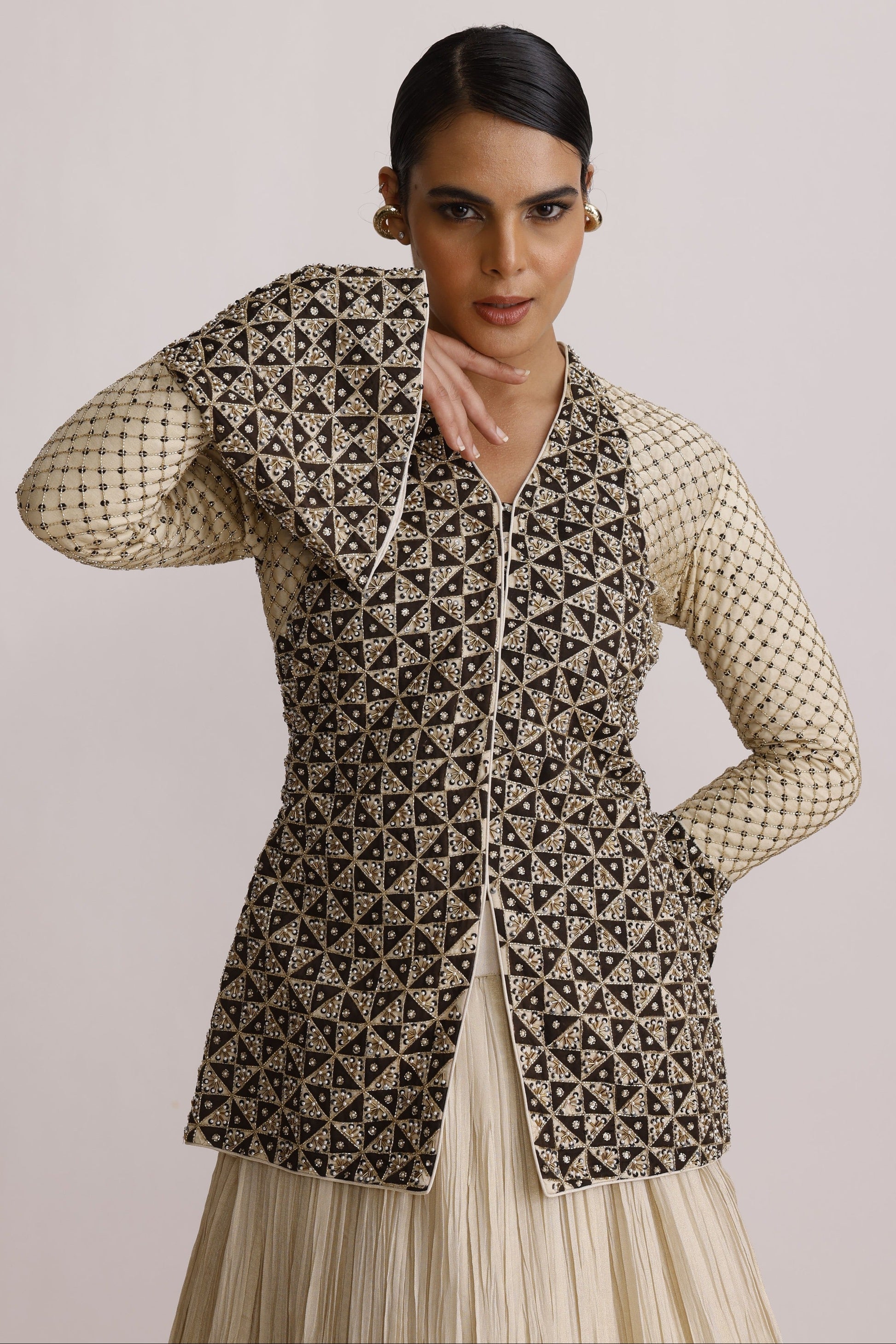A model wearing a sleeveless geometric print vest over a cream-colored long-sleeve top, photographed against a solid light beige background.