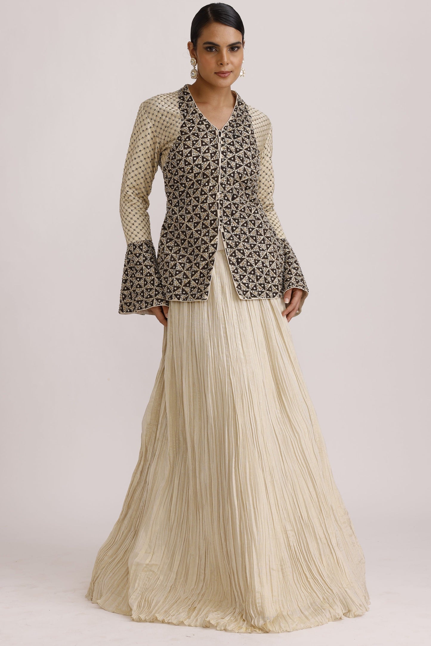 A model wearing a long-sleeved dress with a black and beige geometric patterned top and a pleated cream skirt, shown against a plain light background.