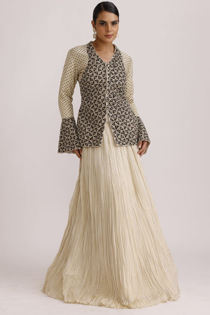 A model wearing a long-sleeved dress with a black and beige geometric patterned top and a pleated cream skirt, shown against a plain light background.