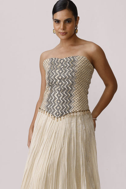 A model wearing a strapless floor-length gown with a pleated cream skirt and a textured, patterned bodice, photographed against a plain light background.