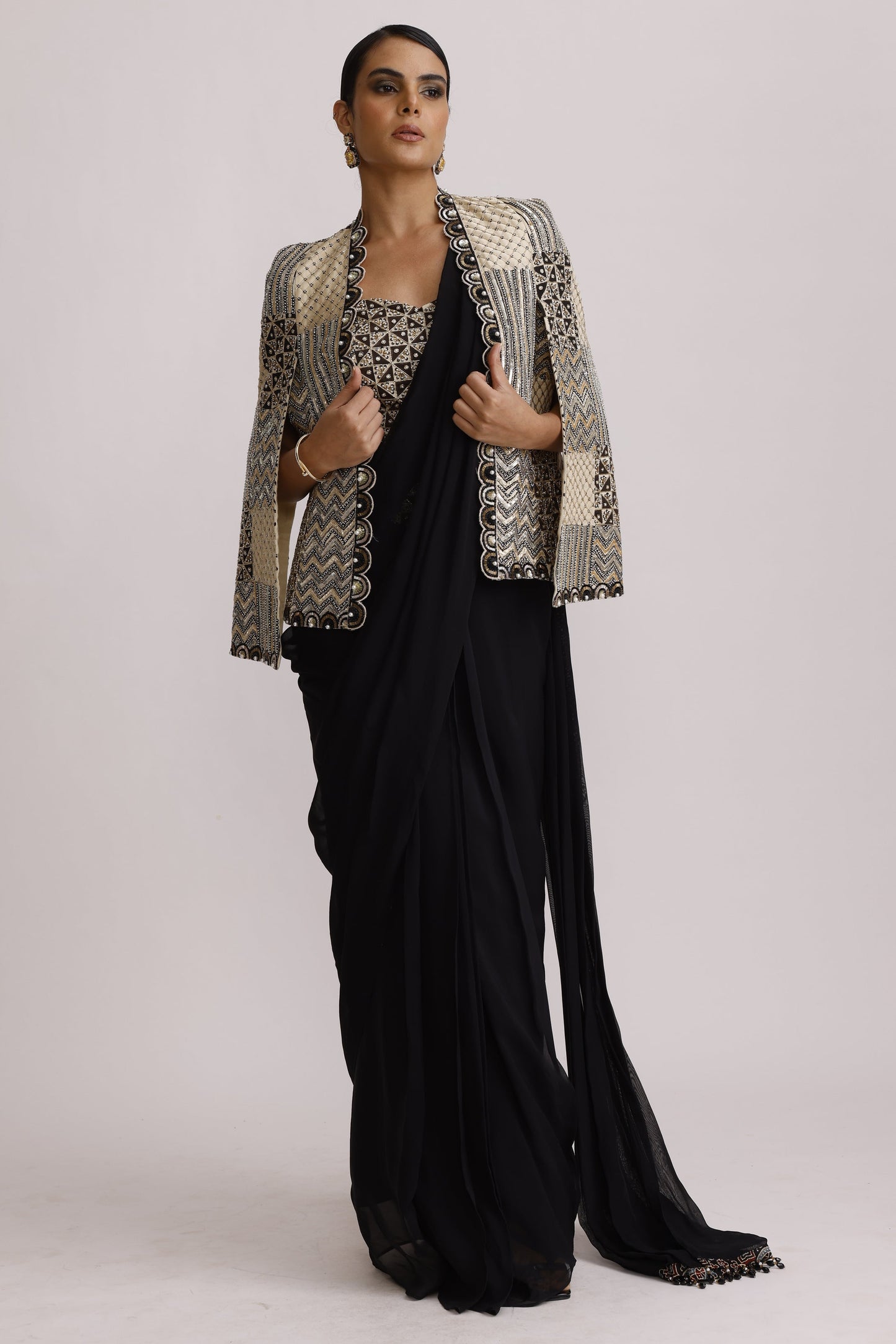 A model wearing a black maxi dress with a silver and black patterned jacket, photographed against a plain light gray studio background.