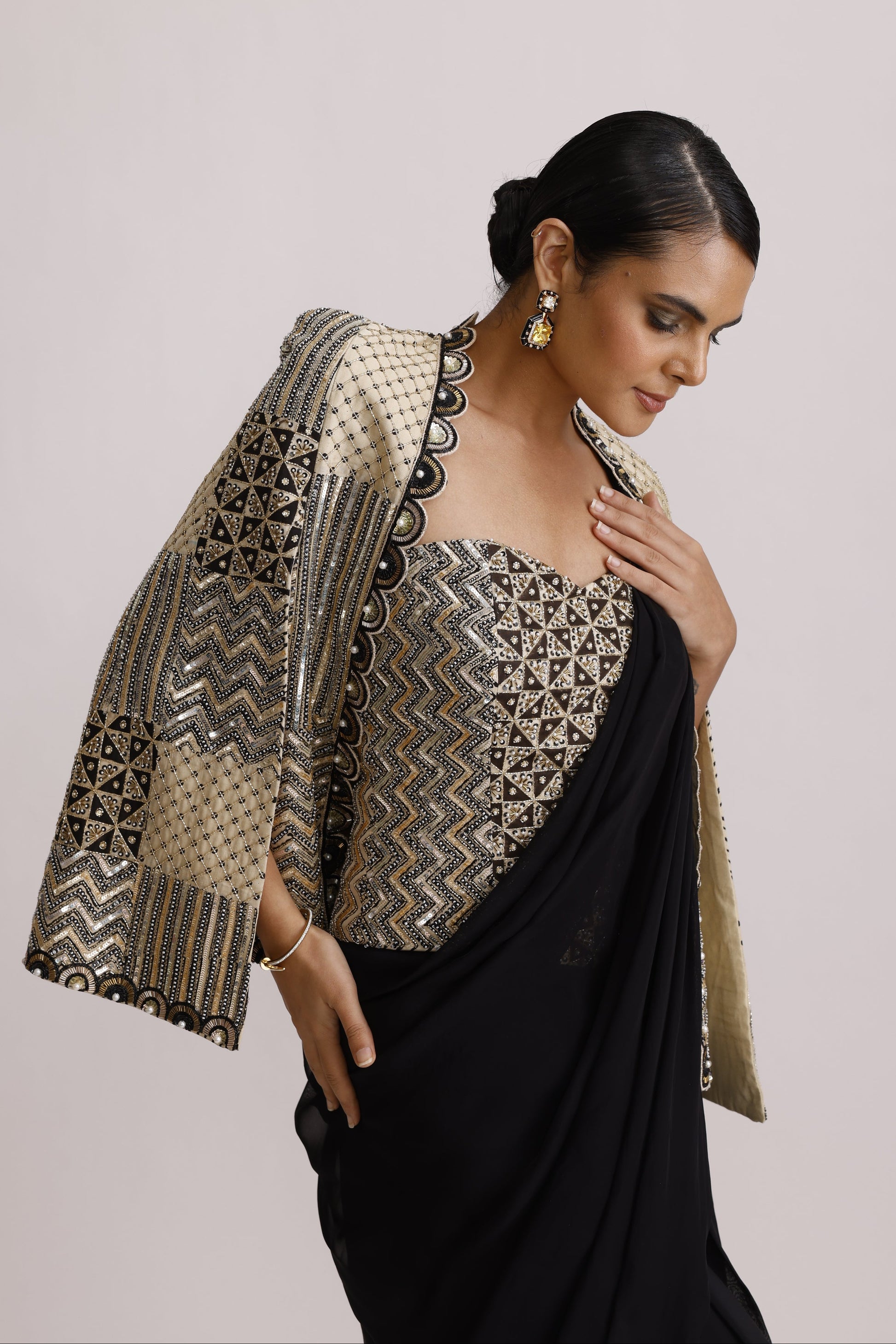 A woman wearing a black kurta with an ornate metallic gold and silver patterned yoke and matching draped fabric, posed against a plain light background.