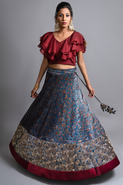 "Explore the allure of indigo Ajrakh print mashru silk lehenga with zardosi & Nakshi embroidery, paired with ruffled blouse & blue organza dupatta"
